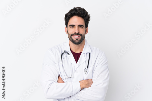 Young handsome man with beard over isolated white background wearing a doctor gown and with arms crossed