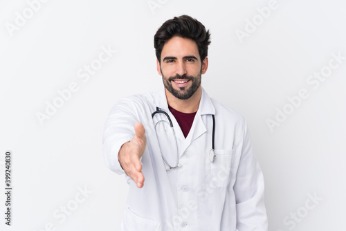 Young handsome man with beard over isolated white background wearing a doctor gown and with stethoscope making a deal