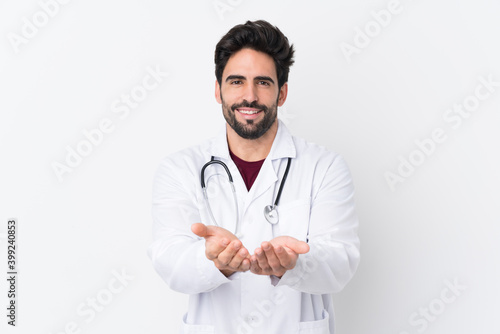 Young handsome man with beard over isolated white background wearing a doctor gown and holding something