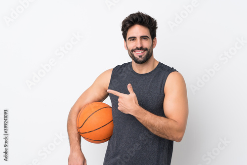 Young handsome man with beard over isolated white background playing basketball and pointing to the lateral © luismolinero