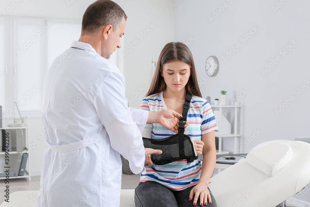 Fototapeta premium Young woman with broken arm visiting doctor in clinic