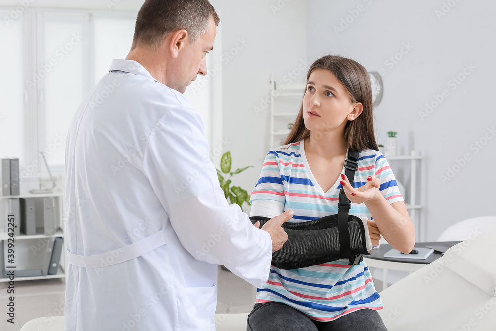 Fototapeta premium Young woman with broken arm visiting doctor in clinic