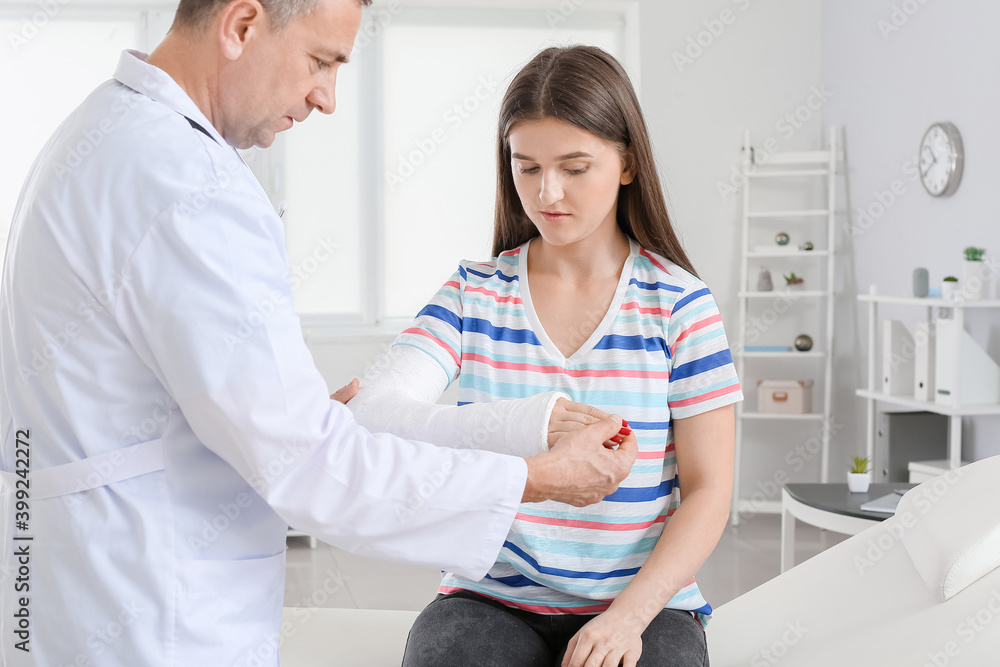 Obraz premium Young woman with broken arm visiting doctor in clinic