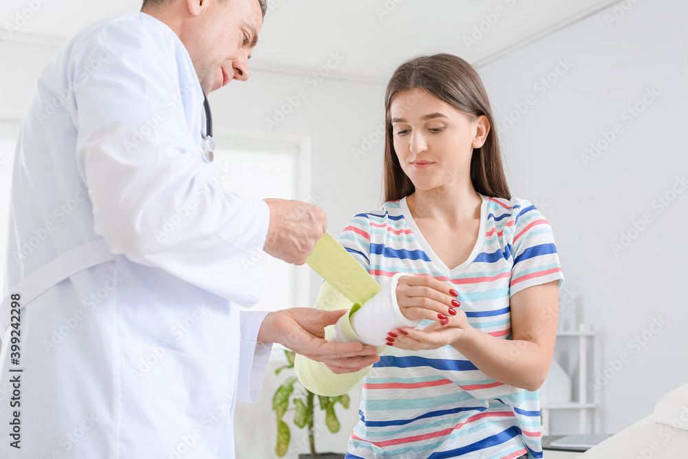Fototapeta premium Young woman with broken arm visiting doctor in clinic