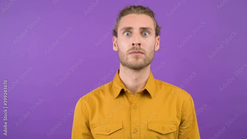 surprised man looks closely at the camera. Young adult isolated on purple background. 4K surprised man looks closely at the camera. Young adult isolated on purple background. 4K