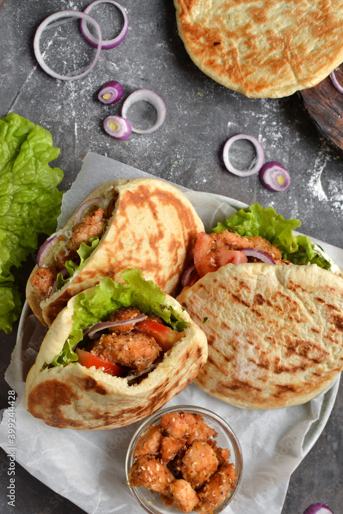 Lavash salad with fried chicken and vegetables. Pita with chicken nuggets, tomatoes, red onions and lettuce and sauce. Healthy fast food. Top view. Dark background. Lavash salad with fried chicken and vegetables. Pita with chicken nuggets, tomatoes, red onions and lettuce and sauce. Healthy fast food. Top view. Dark background.