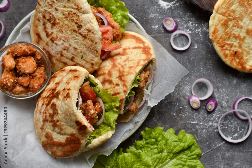 Lavash salad with fried chicken and vegetables. Pita with chicken nuggets, tomatoes, red onions and lettuce and sauce. Healthy fast food. Top view. Dark background.