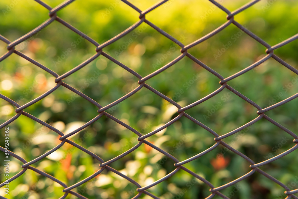 Closeup Industrial wire fence with blurred beautiful garden with natural sunlight and small bokeh background