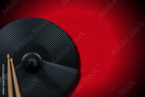 Two wooden drumsticks on a black cymbal of an electronic drum kit, on a red velvet background with copy space. Percussion instrument