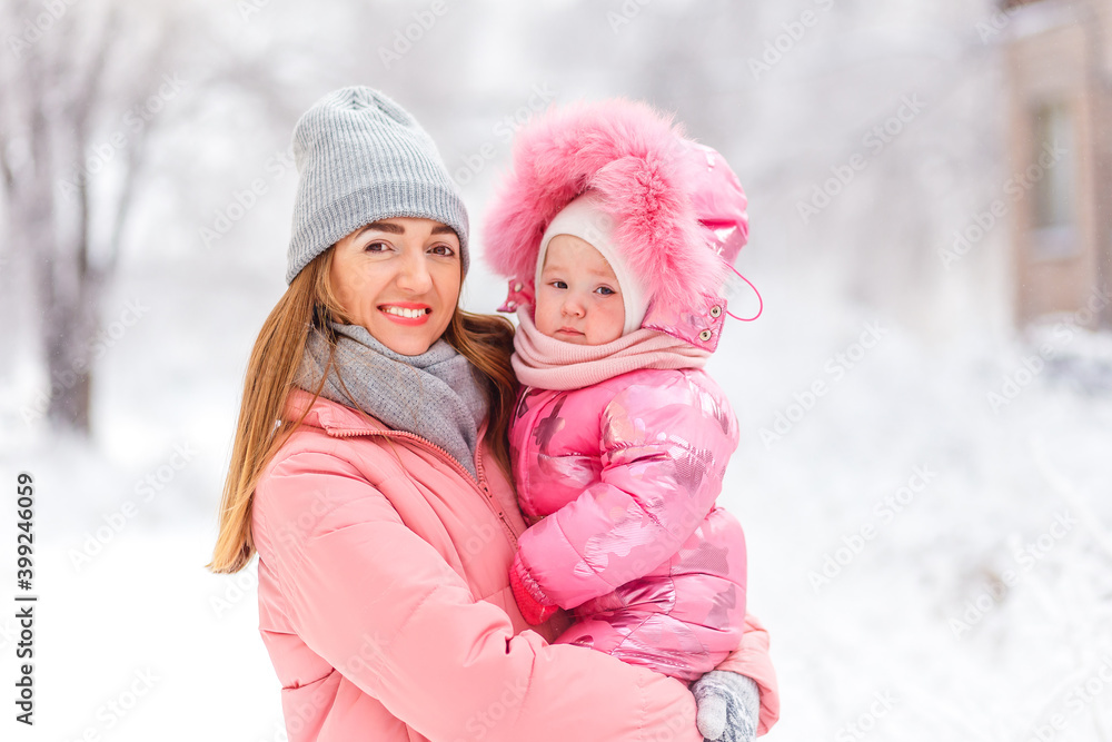 beautiful young smiling woman in pink coat holds a one-year-old baby girl. people ziomy in stylish clothes beautiful young smiling woman in pink coat holds a one-year-old baby girl. people ziomy in stylish clothes