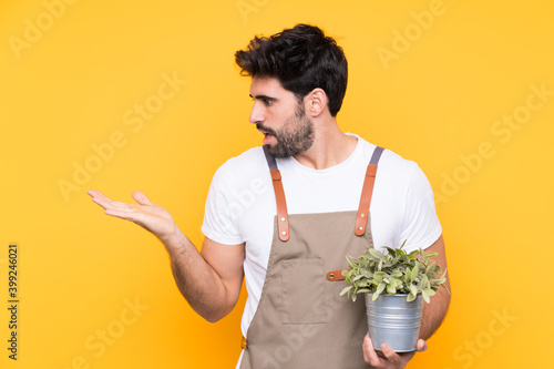 Gardener man with beard over isolated yellow background holding copyspace imaginary on the palm