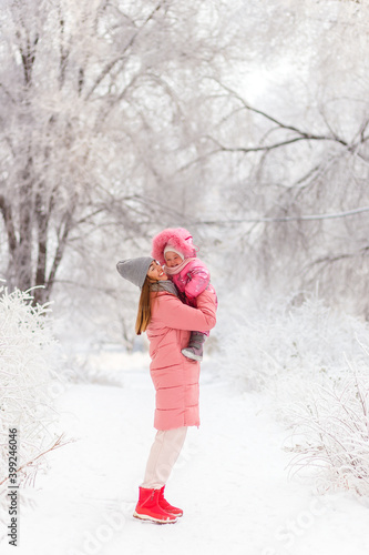 Smiling mother lifts her young daughter in pink winter clothes