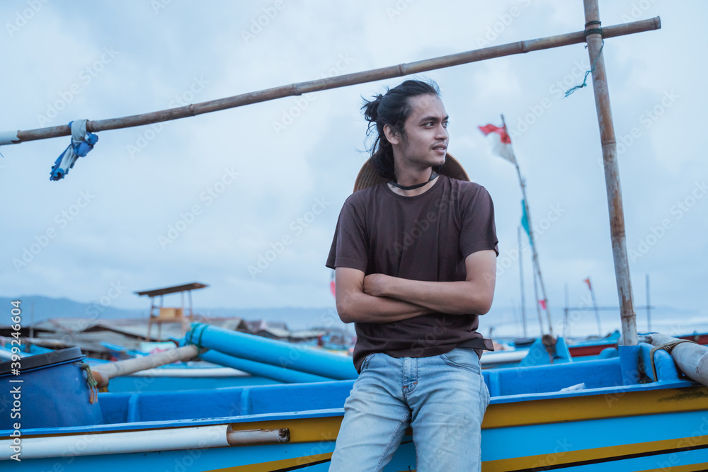 Portrait of a young male fisherman leaning on a boat with cool weather in the background