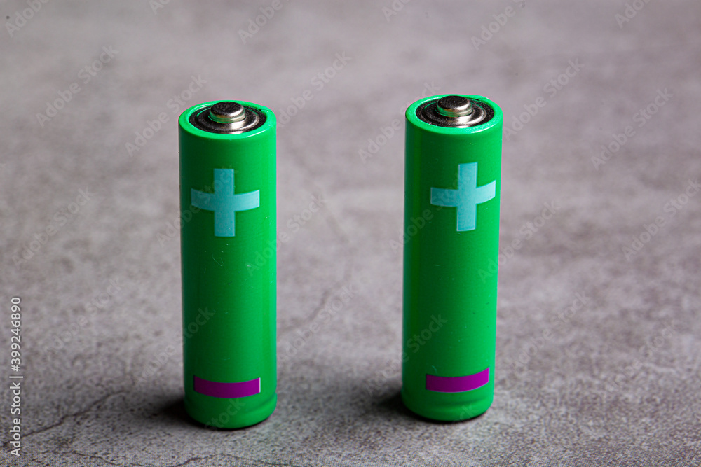 Couple of green double AA batteries isolated on a bright grey background with white positive sign