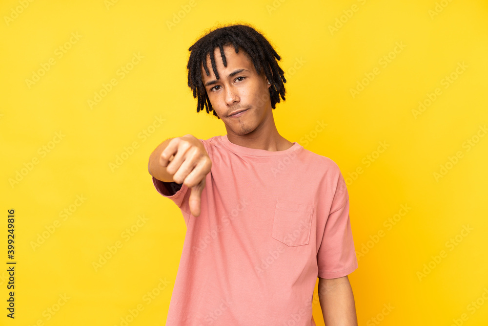 Young african american man isolated on yellow background showing thumb down with negative expression Young african american man isolated on yellow background showing thumb down with negative expression