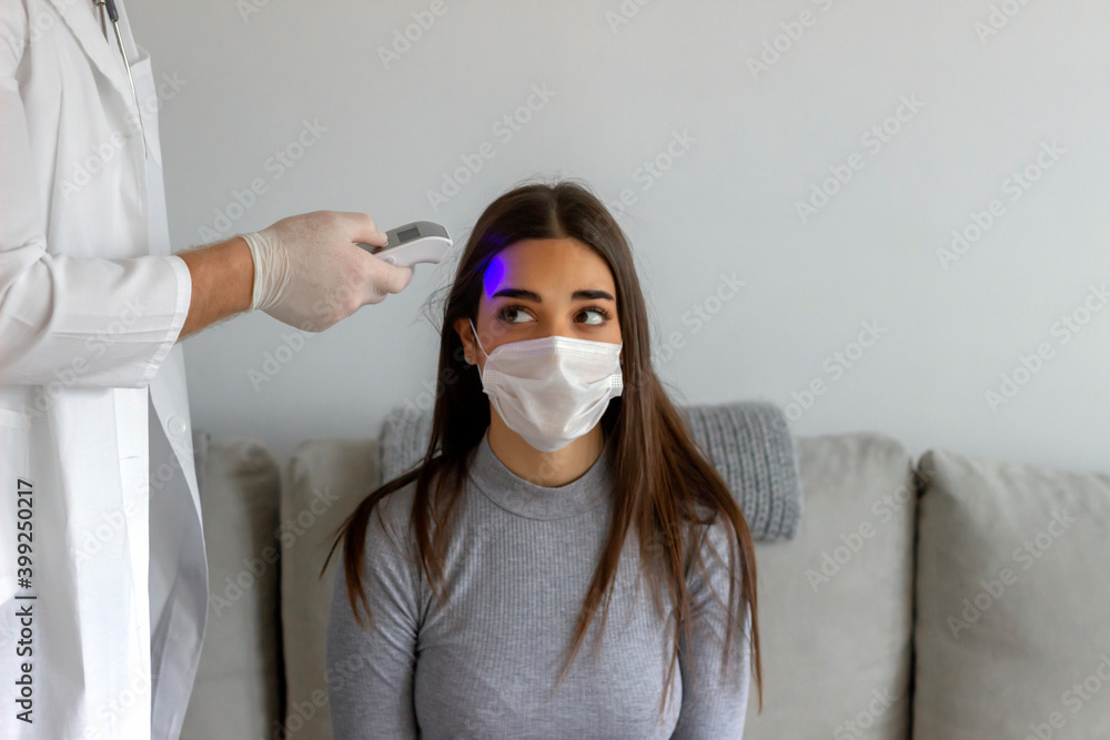 Hand with protective gloves holding infrared thermometer to a woman ...