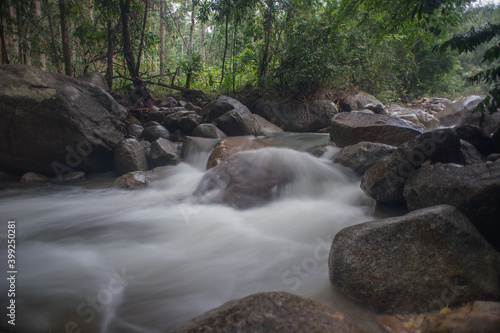 Beautiful waterfall stream in tropical rainforest scenery in the morning in slow shutter mode.Selective focus shot.Image contain grain due to slow shutter shot.