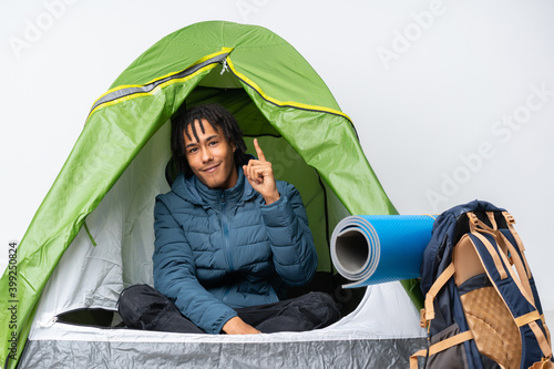 Young african american man inside a camping green tent showing and lifting a finger in sign of the best