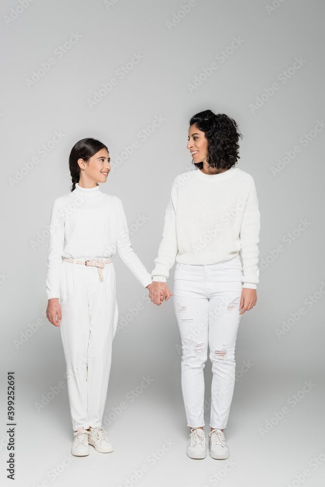 Smiling hipsanic mother and daughter holding hands on grey background, two generations of women Smiling hipsanic mother and daughter holding hands on grey background, two generations of women