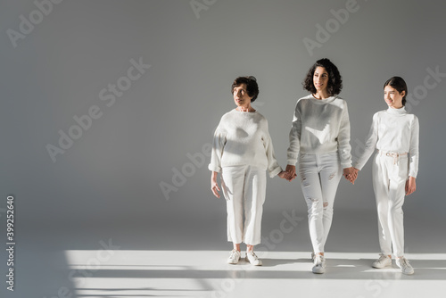 Three generations of hispanic women smiling while walking on grey background © LIGHTFIELD STUDIOS