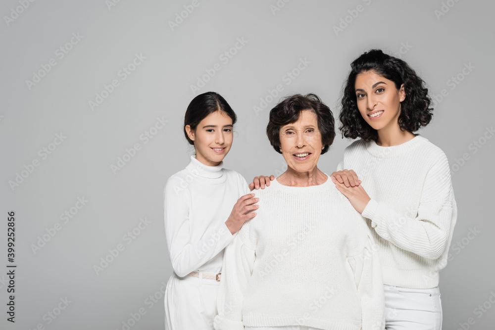 Hispanic woman and daughter embracing smiling grandmother isolated on grey, three generations of women Hispanic woman and daughter embracing smiling grandmother isolated on grey, three generations of women