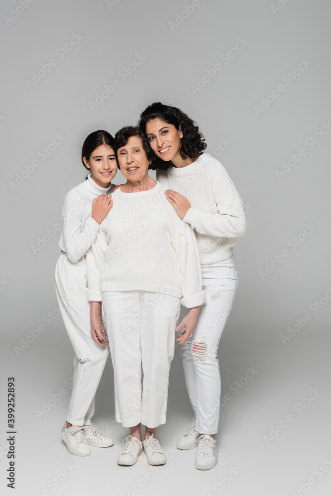 Positive hispanic woman and child hugging granny on grey background, three generations of women Positive hispanic woman and child hugging granny on grey background, three generations of women