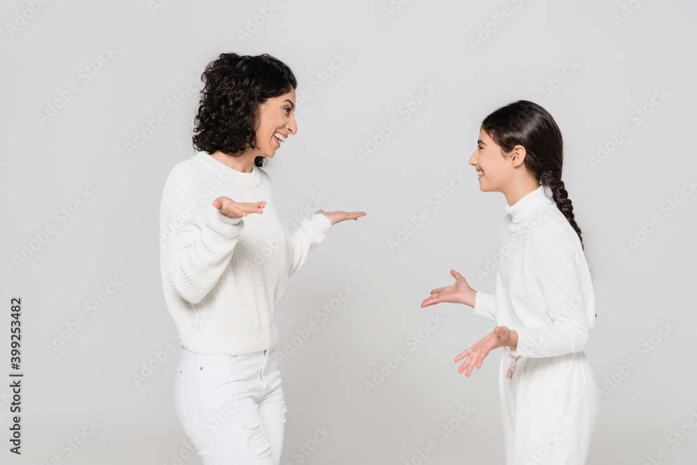 Smiling hispanic woman pointing with hands near cheerful daughter isolated on grey, two generations of women Smiling hispanic woman pointing with hands near cheerful daughter isolated on grey, two generations of women