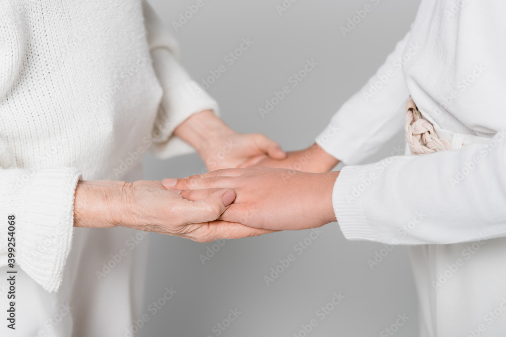 Cropped view of elderly woman and girl holding hands isolated on grey, two generations of women Cropped view of elderly woman and girl holding hands isolated on grey, two generations of women