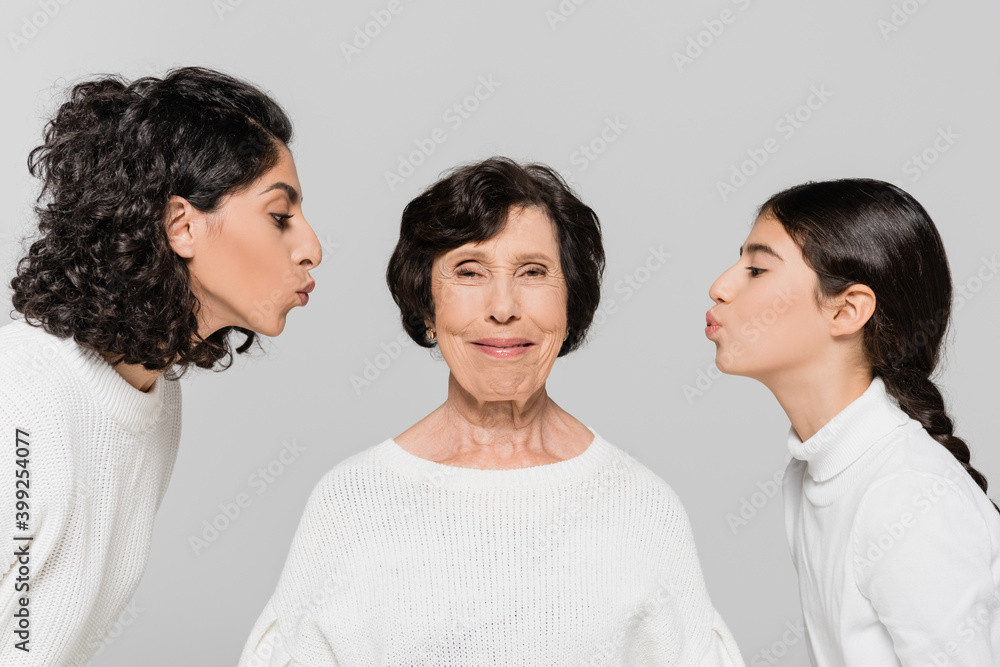 Hispanic woman and girl kissing smiling granny isolated on grey, three generations of women Hispanic woman and girl kissing smiling granny isolated on grey, three generations of women