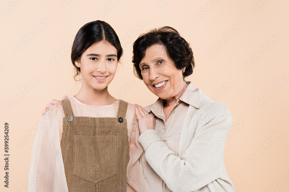 Hispanic granny smiling at camera while embracing granddaughter isolated on beige, two generations of women Hispanic granny smiling at camera while embracing granddaughter isolated on beige, two generations of women