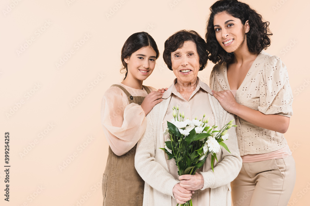 Hispanic mother and daughter hugging grandmother with flowers isolated on beige, three generations of women Hispanic mother and daughter hugging grandmother with flowers isolated on beige, three generations of women