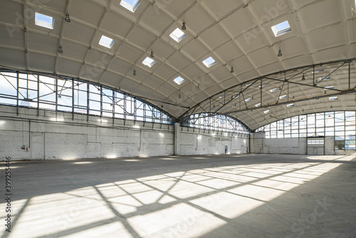 Huge empty industrial warehouse. White interior. Unique architecture. Hemispherical reinforced concrete load bearing roof with windows. Shadow of construction on floor. © Aleks Kend