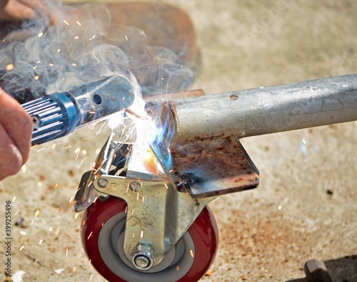 Worker with a welding machine fixing a caster wheels, sparks flying around