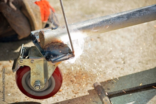 Worker with a welding machine fixing a caster wheels, sparks flying around