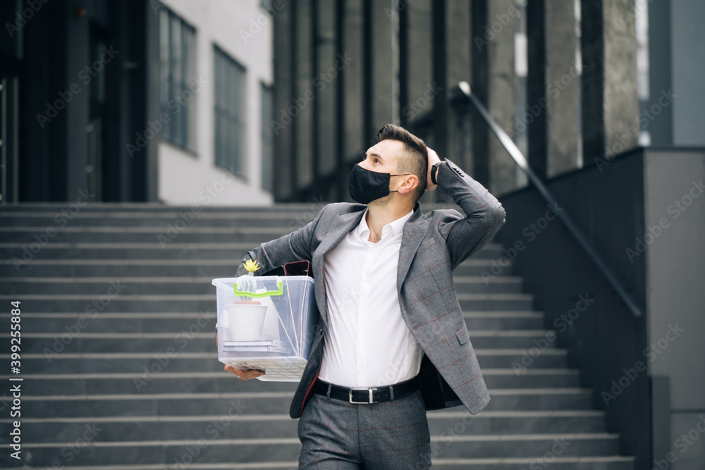 Fototapeta premium Sad male office worker in depression with box of personal stuff. Businessman lost job. Fired man walking outdoor. Depressed jobless person. Unemployment concept. Left without money.