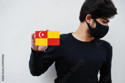 Malay man wear all black with face mask hold Selangor flag in hand isolated on white background. States and federal territories of Malaysia coronavirus country concept. photo