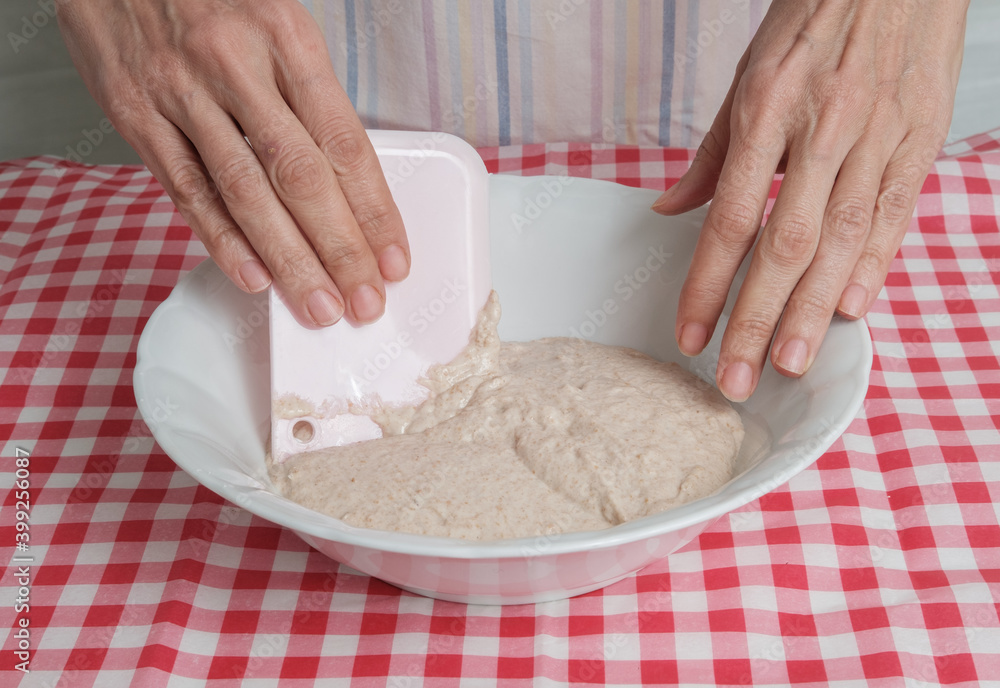 Fototapeta premium Kneading a dough of bread in a bowl. Female hands working. Making pizza. Cooking at home. Homemade food. Italian cloth.