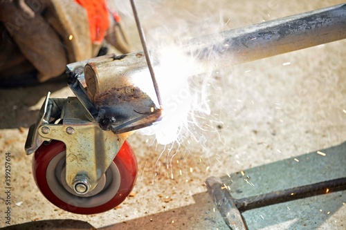 Worker with a welding machine fixing a caster wheels, sparks flying around