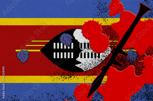 Swaziland flag and black RPG-7 rocket-propelled grenade launcher in red blood. Concept for terror attack or military operations with lethal outcome photo