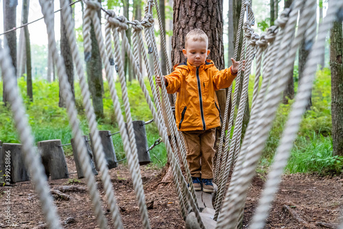 Young Child Playing on Rope Obstacle Track in Woods - Caucasian Boy Wearing Orange Raincoat