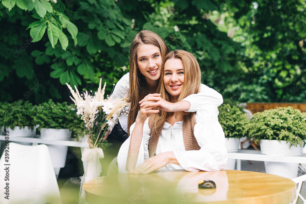 Naklejka premium Joyful adult daughter hugs her mother and holds flowers for her. Birthday surprise for mom