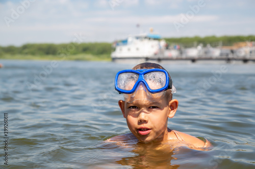 a boy with a diving mask stands in the water against the background of a passing ship © vitec40