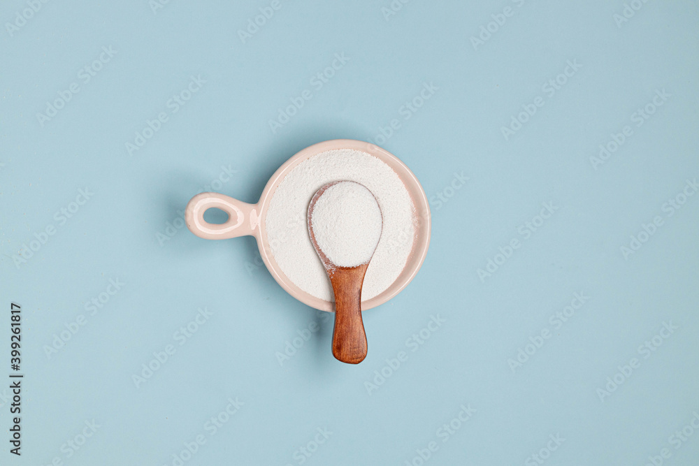 Collagen powder in a glass bowl and small wooden spoon on blue background. Top view, space for text. Healthy lifestyle concept. Horizontal minimal banner