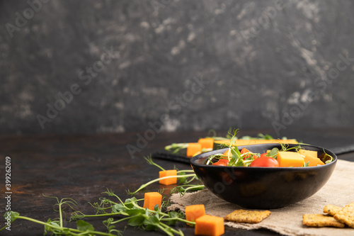 Vegetarian vegetable salad of tomatoes, pumpkin, microgreen pea sprouts on black concrete background. Side view, copy space.