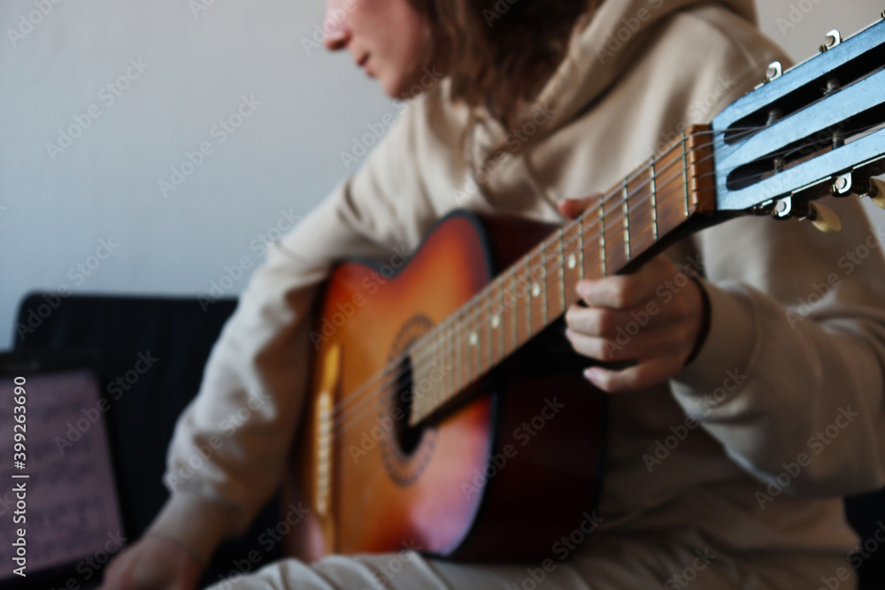 Fototapeta premium A girl is playing the guitar and watching notes on a laptop. 