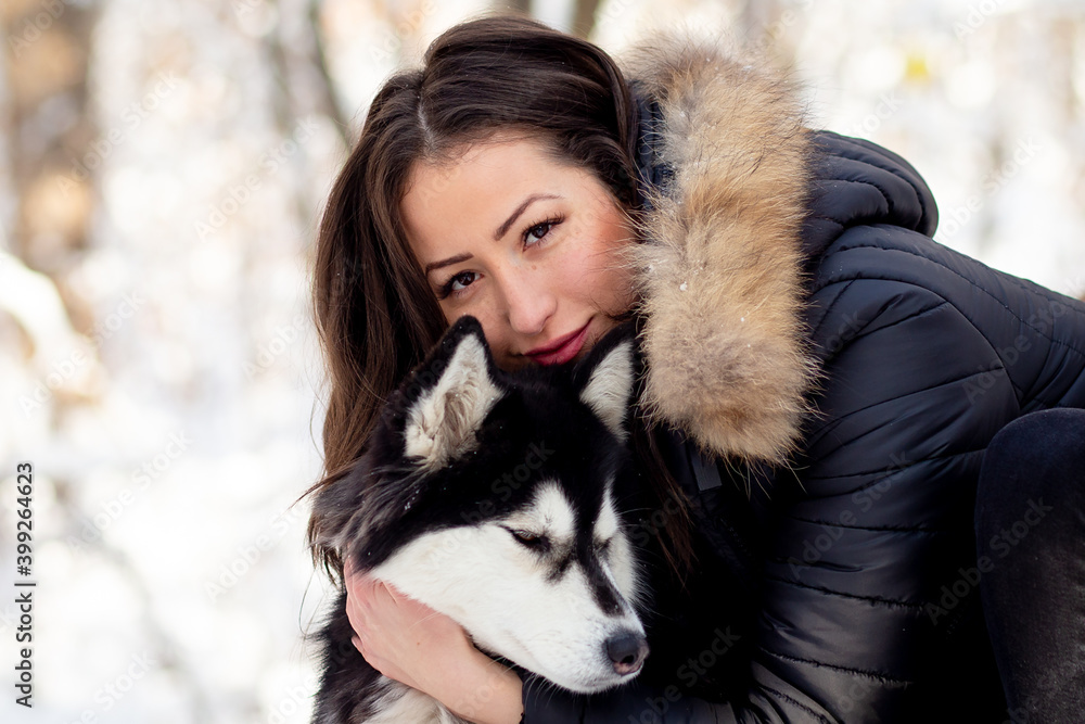 Beautiful young woman hugging female husky dog in cold winter snowy day Beautiful young woman hugging female husky dog in cold winter snowy day