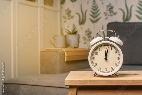 Alarm clock stands on a wooden table in living room with a modern interior with green plants