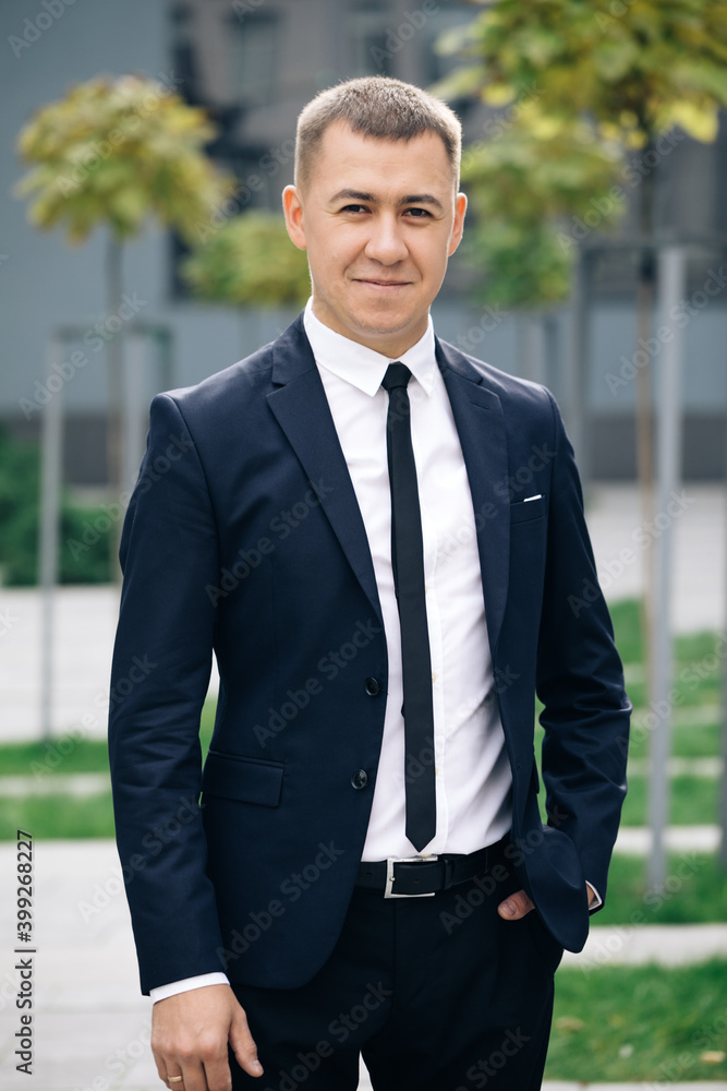 Portrait of handsome man in tie smiling cheerfully to camera at street near business center. Happy cheerful man looking straight with smile. Successful career attractive manager handsome confident Portrait of handsome man in tie smiling cheerfully to camera at street near business center. Happy cheerful man looking straight with smile. Successful career attractive manager handsome confident