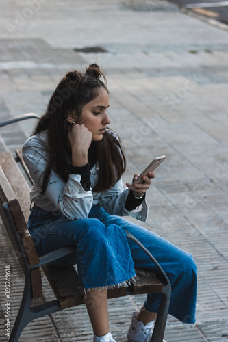 woman waiting for the bus, looking at the mobile phone, sitting on a bench