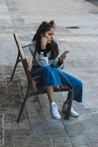woman waiting for the bus, looking at the mobile phone, sitting on a bench